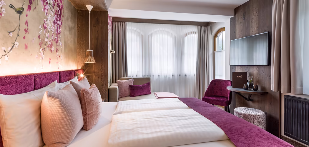 In beeren Farbe gehaltener Raum mit Doppelbett, Couch und TV