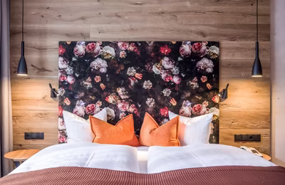 Holztäfelung hinter dem Bett, florales Rückenteil mit orangen Zierkissen auf dem Doppelbett