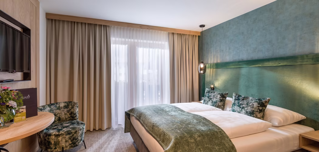 Zimmer in grün gehalten mit Doppelbett und Sitzmöglichkeit